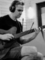 Na zdjęciu mężczyzna w słuchawkach gra na gitarze w studiu nagraniowym