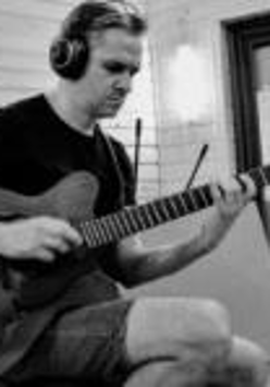 Na zdjęciu mężczyzna w słuchawkach gra na gitarze w studiu nagraniowym