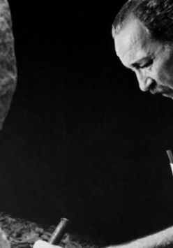 Na czarno-białym zdjęciu artysta rzeźbiący w kamieniu.