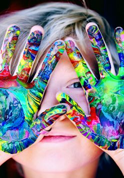 Twarz chłopca zasłaniają pomalowane róznymi kolorami ręce.