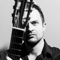 Na zdjęciu twarz mężczyzny. Prawą stronę twarzy przesłania mu gryf gitary.