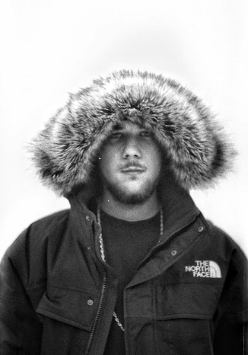 Na zdjęciu młody mężczyzna w zimowej kurtce z założonym na głowę kapturem.