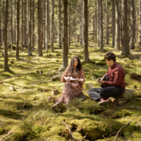 Na zdjęciu dwie osoby siedzące na polanie w lesie.