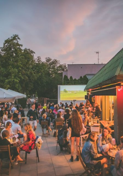 Ludzie siedzą wieczorem przy stolikach, rozmawiają.