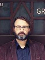 Na zdjęciu mężczyzna z brodą na tle drzwi.