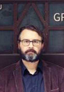 Na zdjęciu mężczyzna z brodą na tle drzwi.