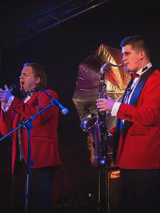 Dwójka mężczyzn. ubranych na czerwono, jedna śpiewa drugi gra na saksofonie.