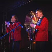 Dwójka mężczyzn. ubranych na czerwono, jedna śpiewa drugi gra na saksofonie.