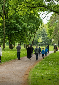 Zdjęcie w środku parku, przedstawiające grupkę ludzi idących ścieżką w parku.