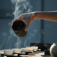 Zdjęcie przedstawiające rękę lejącą herbatę do ułożonych w rzędzie filiżanek.