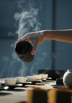 Zdjęcie przedstawiające rękę lejącą herbatę do ułożonych w rzędzie filiżanek.