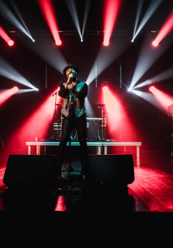 Na zdjęciu artysta śpiewający na scenie na tle czerwono białych świateł.