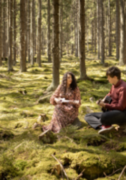 Na zdjęciu członkowie zespołu siedzący na trawie w lesie.