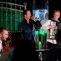 Na zdjęciu trzyosobowy zespół muzyczny na scenie.