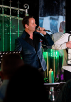 Na zdjęciu trzyosobowy zespół muzyczny na scenie.