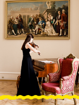 Na zdjęciu skrzypaczka stojąca przy fortepianie. Na ścianie obraz przedstawiający scenę z życia dworu.