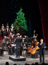 Na zdjęciu scena i muzycy podczas koncertu w aulii UAM. Na środku sceny stoi choinka.
