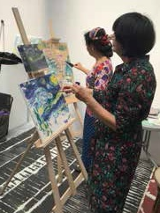 Dwie kobiety malujące obrazy na sztalugach.