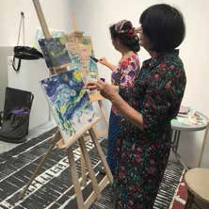 Dwie kobiety malujące obrazy na sztalugach.