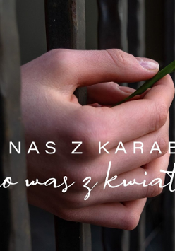 Na zdjęciu ręce z przebiśniegiem wystające zza krat. Na nadgarstku lewej ręki biało-czerwono-biała opaska.