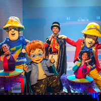 Zdjęcie ze spektaklu; na scenie stoją aktorzy przebrani za strażaków, baletnice, chłopiec w okularach oraz wąsaty pan w kapeluszu