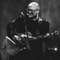 Na czarno-białym zdjęciu postać Roberta Kasprzyckiego z gitarą.