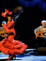 Na zdjęciu tancerka na scenie w tle siedzący mężczyzna z gitarą.