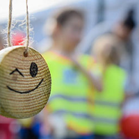 zdjęcie drewnianego medalu z narysowanym uśmiechem; w tle widoczne dzieci biorące udział w biegu