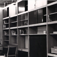 Czarno-białe zdjęcie drewnianej meblościanki. Na półkach widoczne są książki i stare radio.
