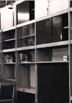 Czarno-białe zdjęcie drewnianej meblościanki. Na półkach widoczne są książki i stare radio.