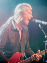 Na zdjęciu Andy Egert z gitarą śpiewa do mikrofonu.