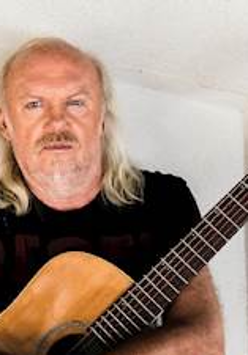 Na zdjęciu artysta stojący z gitarą.