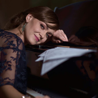 Na zdjęciu artystka opierająca twarz o fortepian.