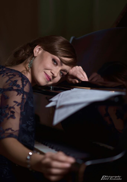 Na zdjęciu artystka opierająca twarz o fortepian.