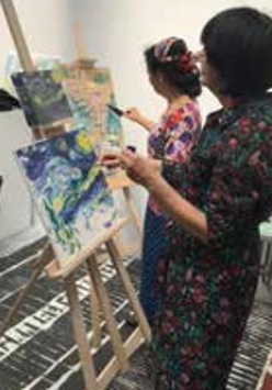 Dwie kobiety malujące obrazy na sztalugach.