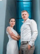 Fotografia pary artystów stojących na tle nowoczesnej, modernistycznej architektury.