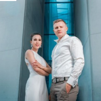 Fotografia pary artystów stojących na tle nowoczesnej, modernistycznej architektury.