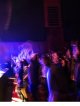 Artystycznie rozmyte zdjęcie z zamkowego koncertu w Sali Wielkiej. Roztańczona publiczność przed zamkową sceną oświetloną kolorowym światłem.