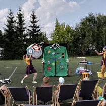 Kobieta i mężczyzna rzucający wielką kostką szcześcienną podczas zabawiania dzieci.