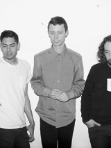 Czarno-białe zdjęcie trójki mężczyn stojących pod ścianą.