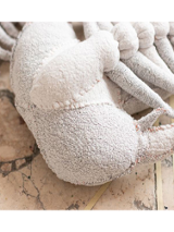 Zbliżenie na jasną formę przypominającą fragment szkieletu na beżowym kamiennym tle. Przedmiot wydaje się stworzony ręcznie - na brzegach dostrzec można regularne szwy.