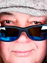 Na zdjęciu Stanisław Soyka w kaszkiecie na głowie i trzymający okulary przed twarzą.