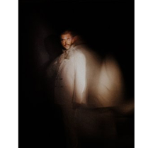 Rozmazana sylwetka artysty na ciemnym tle.