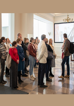Uczestnicy stoją w holu Biblioteki i słuchają przewodnika.
