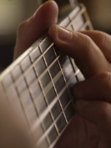 Zdjęcie gryfu i dłoni z chwytem gitarowym.