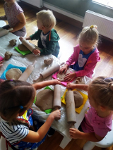 Zdjęcie przedstawia grupkę małych dzieci wałkujących kawałki gliny.