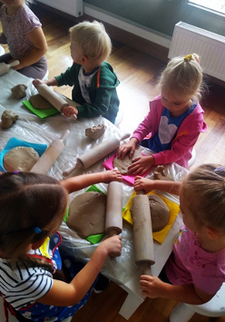 Zdjęcie przedstawia grupkę małych dzieci wałkujących kawałki gliny.