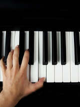 Dłoń na klawiszach fortepianu.