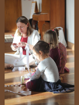 Zdjęcie przedstawia grupę małych dzieci na warsztatach wraz z prowadzącą.