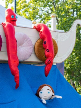 Zdjęcia maskotki ze spektaklu. Imitacja dziecka w wodzie, a obok na białej łodzi kraken.